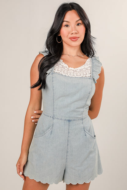 Woman wearing a light blue denim romper with lace details on a plain background