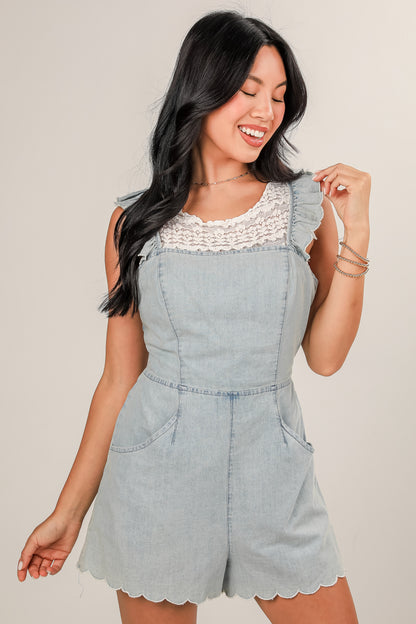 Woman wearing a light blue denim romper with lace details on a plain background