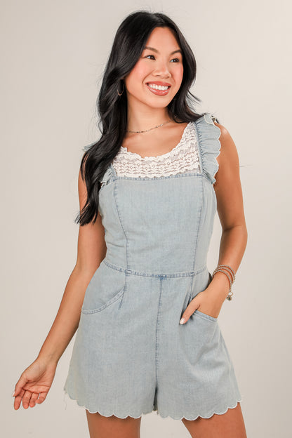 Woman wearing a light blue denim romper with lace details on a plain background