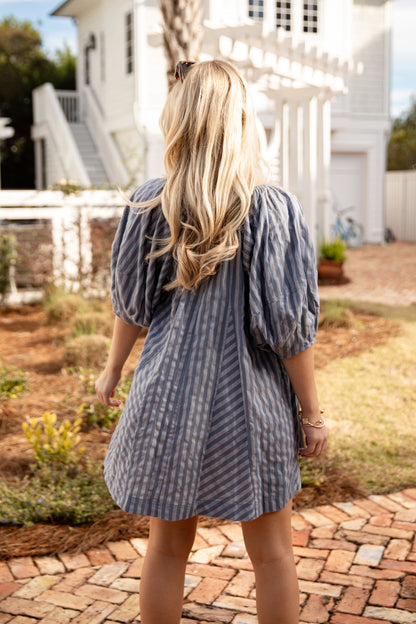 Woman in a blue striped dress standing on a brick path with a white house in the background