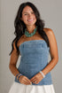 A woman wearing a light blue denim strapless tube top and a white skirt, accessorized with a chunky green beaded necklace and bracelets, posing against a light gray wall.