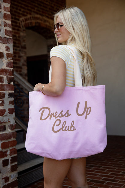 A woman with blonde hair and sunglasses carries a large lavender tote bag with &