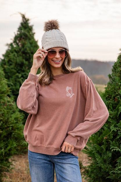 Woman wearing a pink sweatshirt with a logo, sunglasses, and a beanie outdoors.