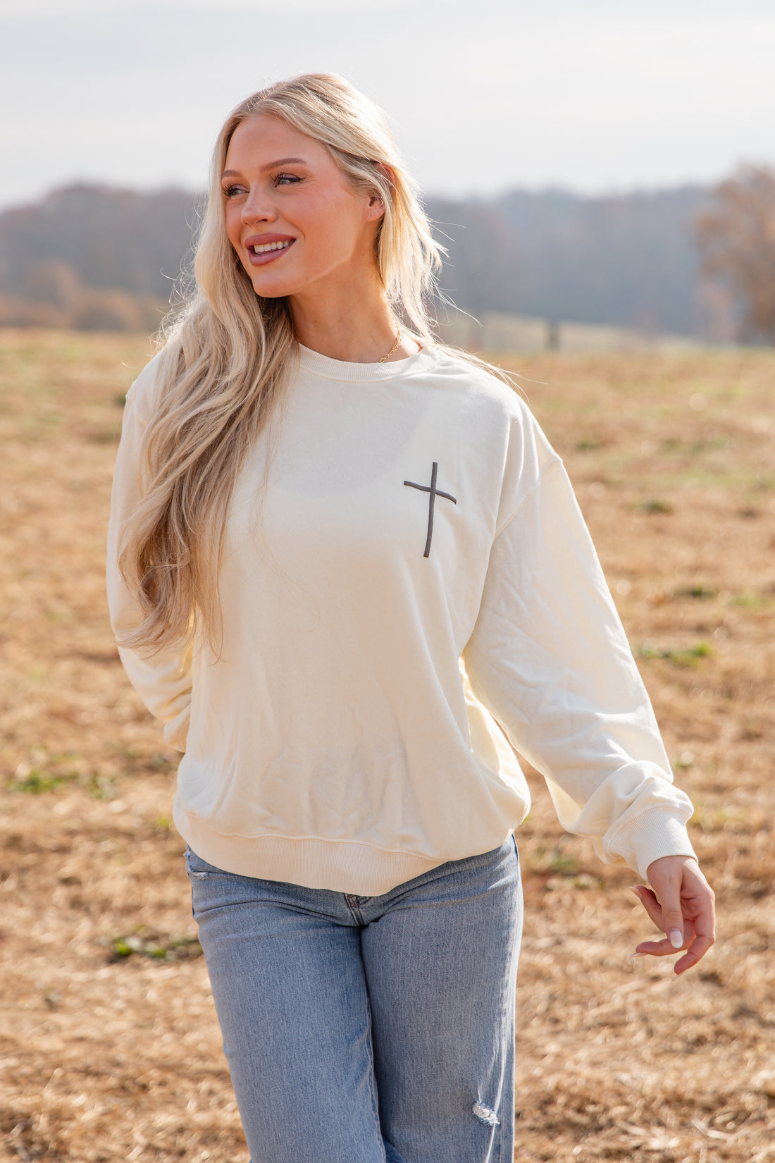 Woman wearing a beige sweatshirt with a cross design in a field
