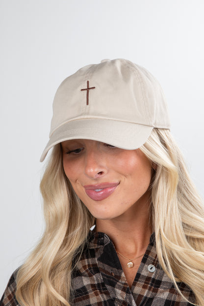 Woman wearing a beige cap with a cross emblem on a plain background