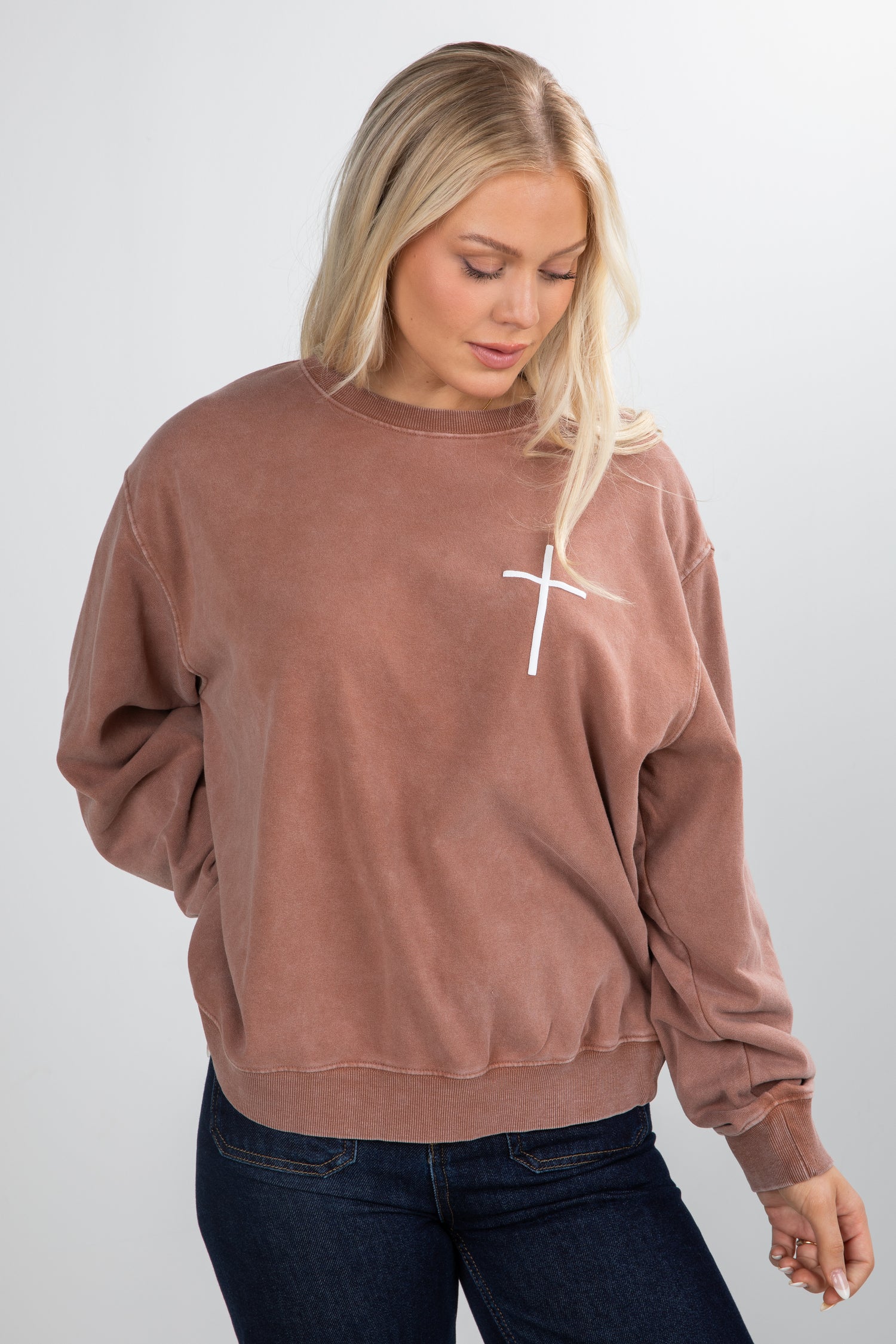 Woman wearing a brown sweatshirt with a white cross design on a plain background