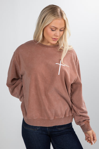 Woman wearing a brown sweatshirt with a white cross design on a plain background