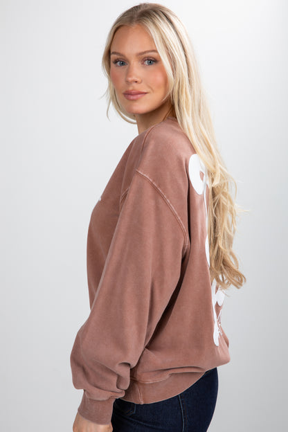 Woman wearing a brown sweatshirt with white designs on a plain background