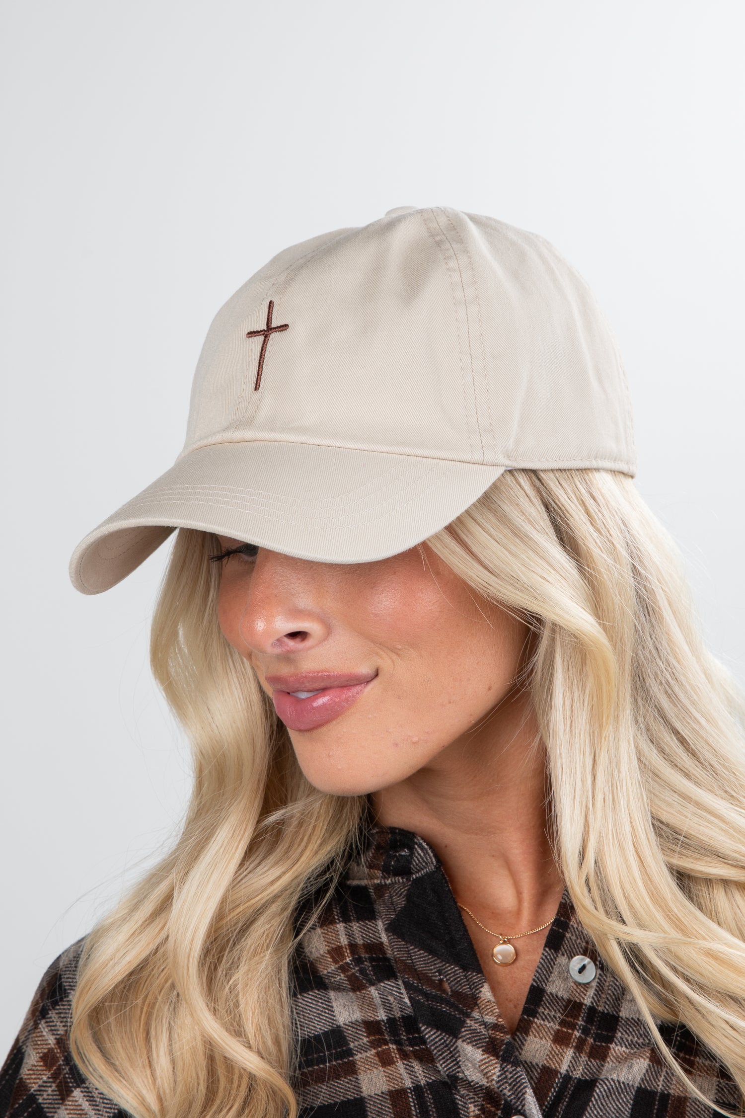 Woman wearing a beige cap with a cross emblem on a plain background