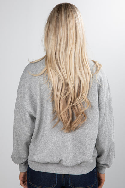 Person wearing a gray hoodie with long blonde hair, standing against a plain background