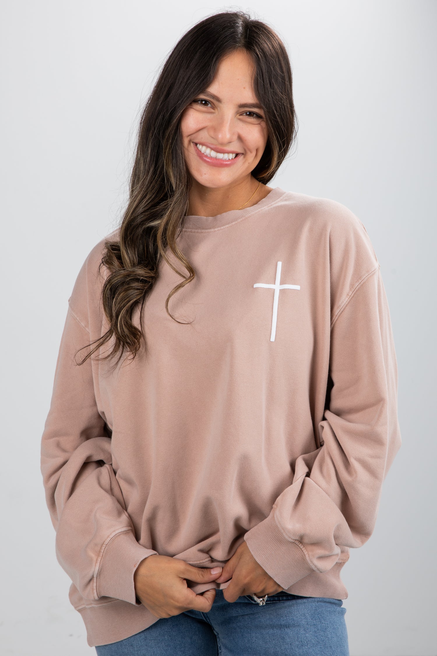 Woman wearing a beige sweatshirt with a white cross design on a plain background