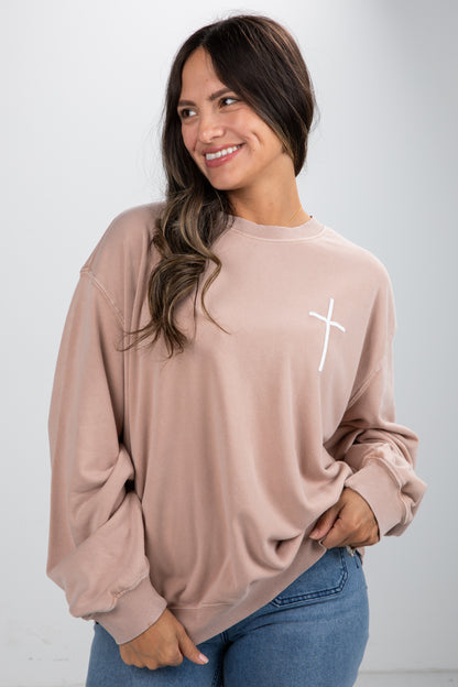 Woman wearing a beige sweatshirt with a white cross design on a plain background