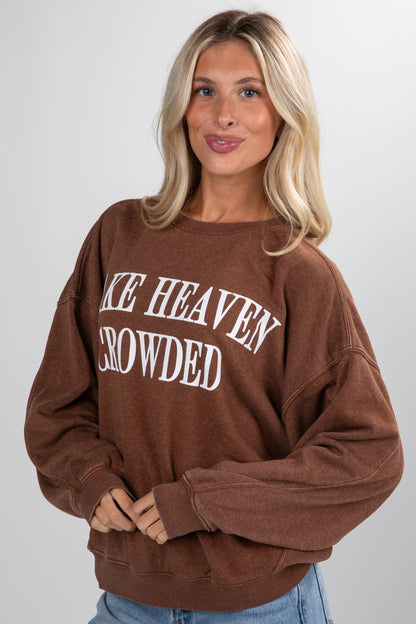 Woman wearing a brown sweatshirt with text, standing against a plain background