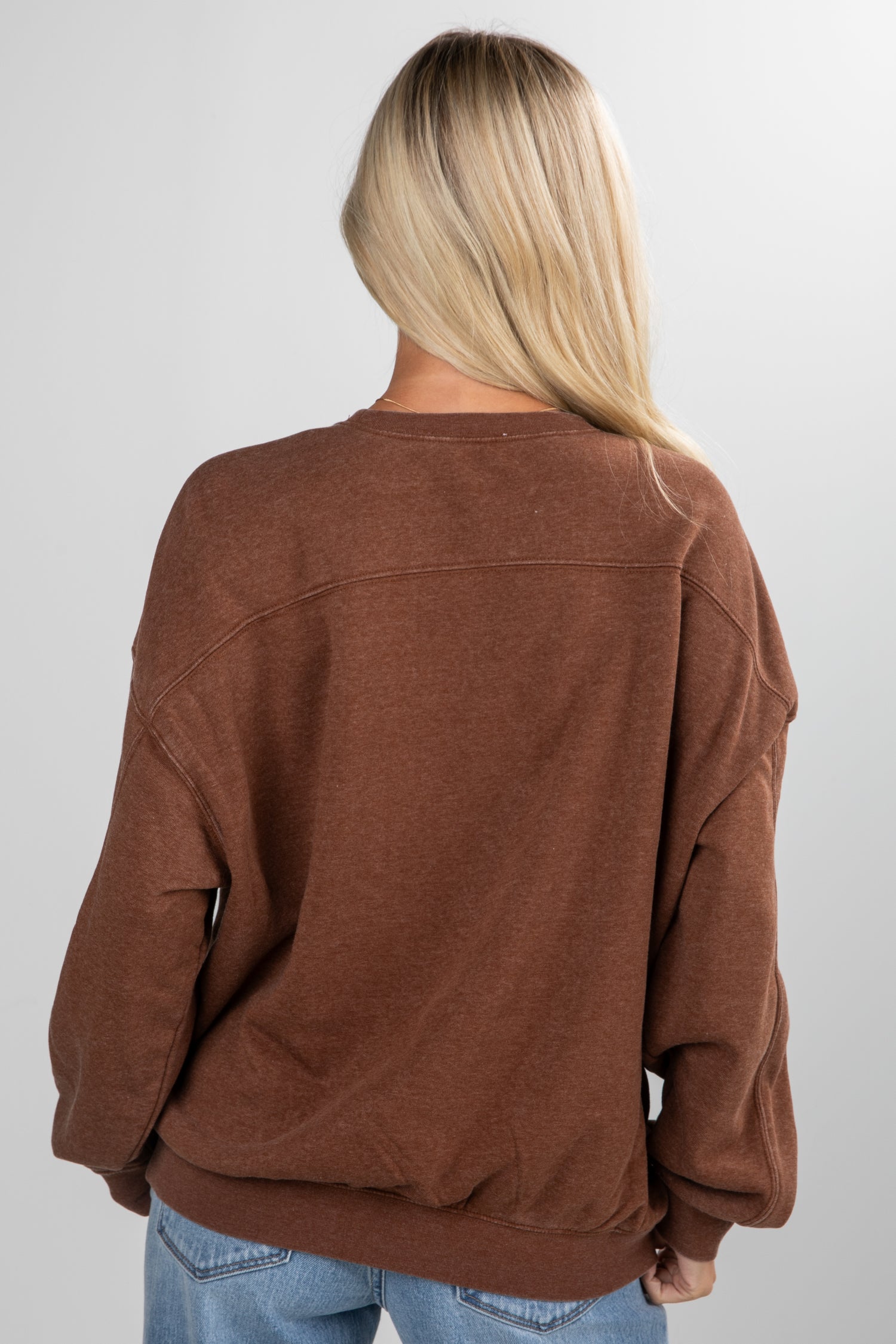 Person wearing a brown sweater and blue jeans on a plain background