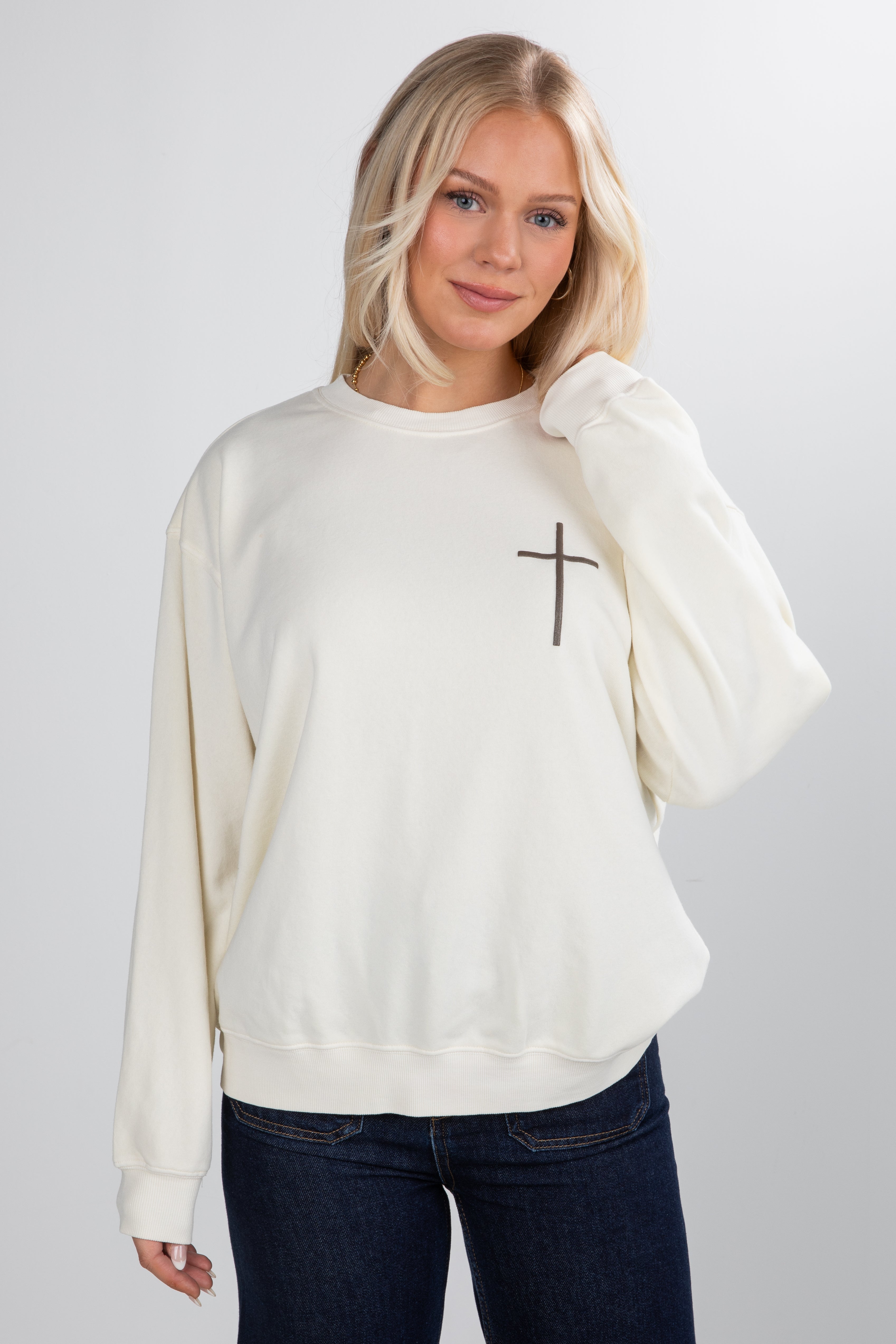 Woman wearing a cream sweatshirt with a black cross design on a plain background