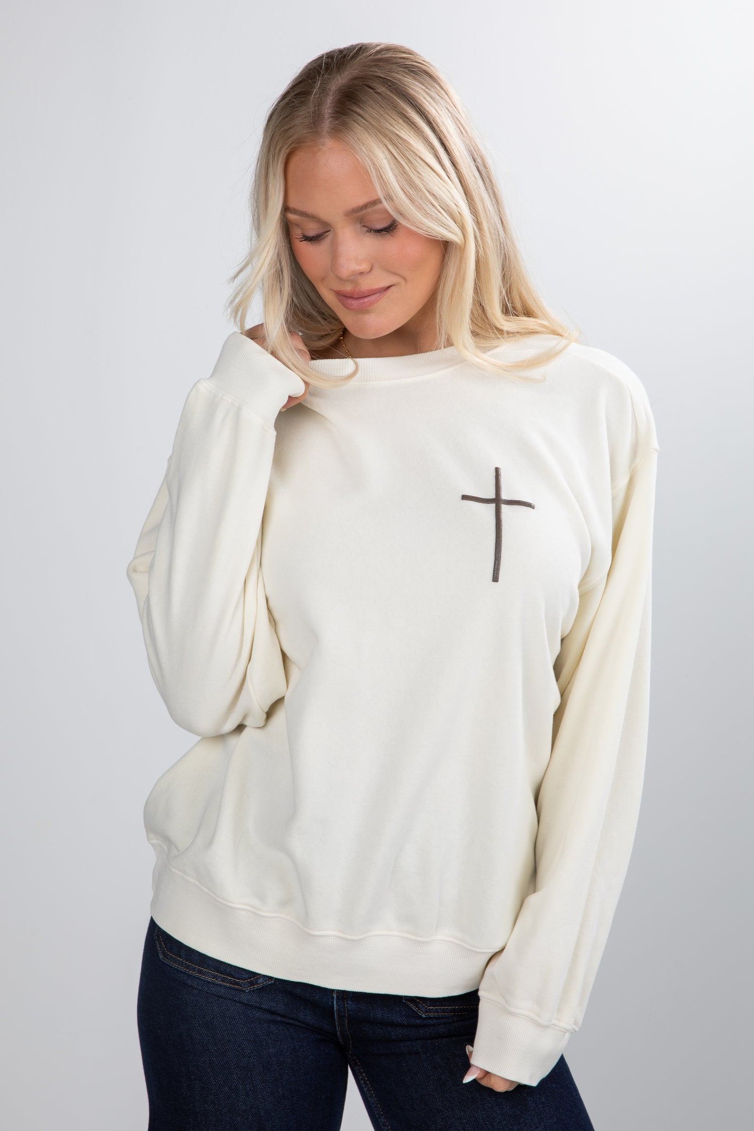 Woman wearing a white sweatshirt with a cross design on a plain background