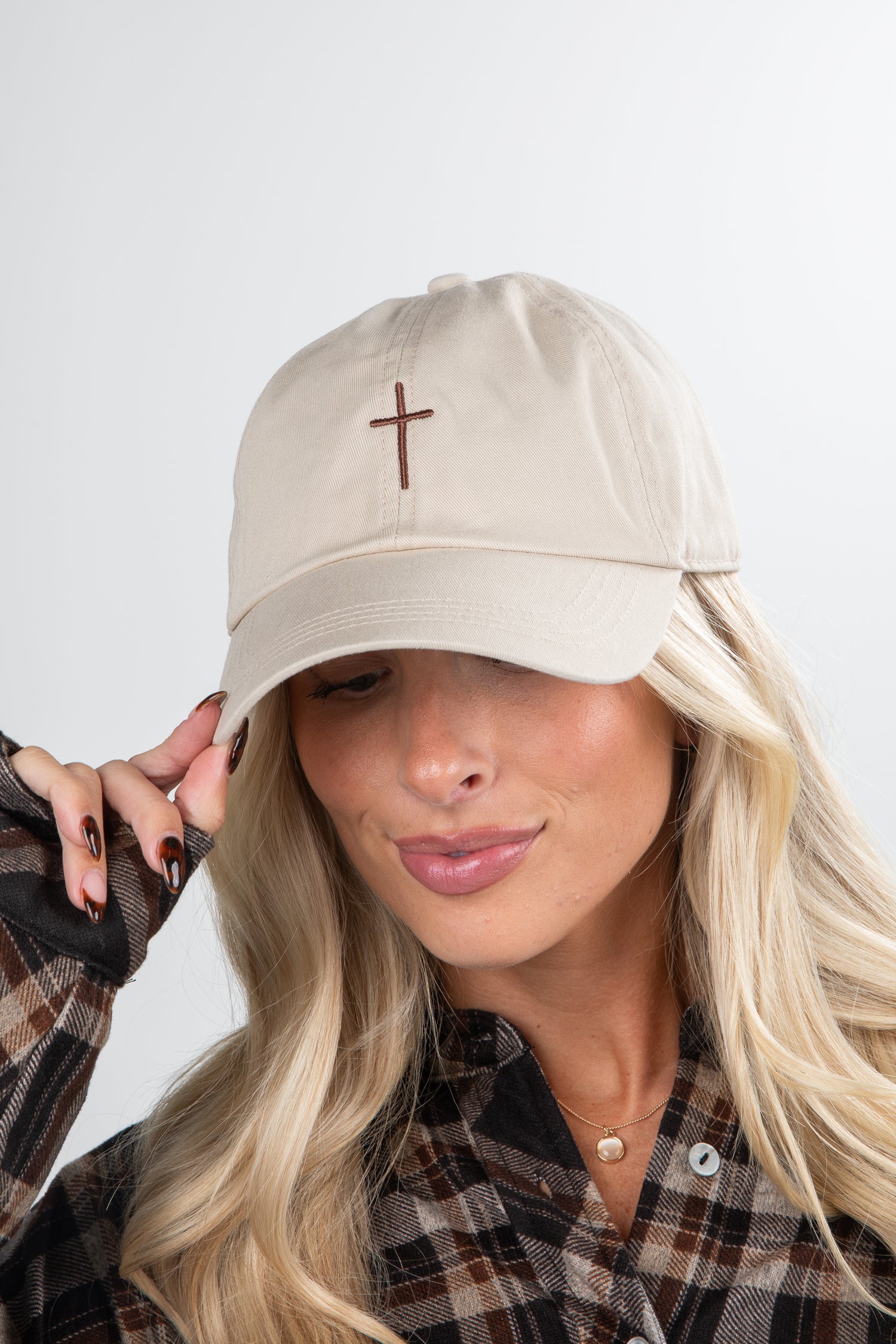 Woman wearing a beige cap with a brown cross on a plain background