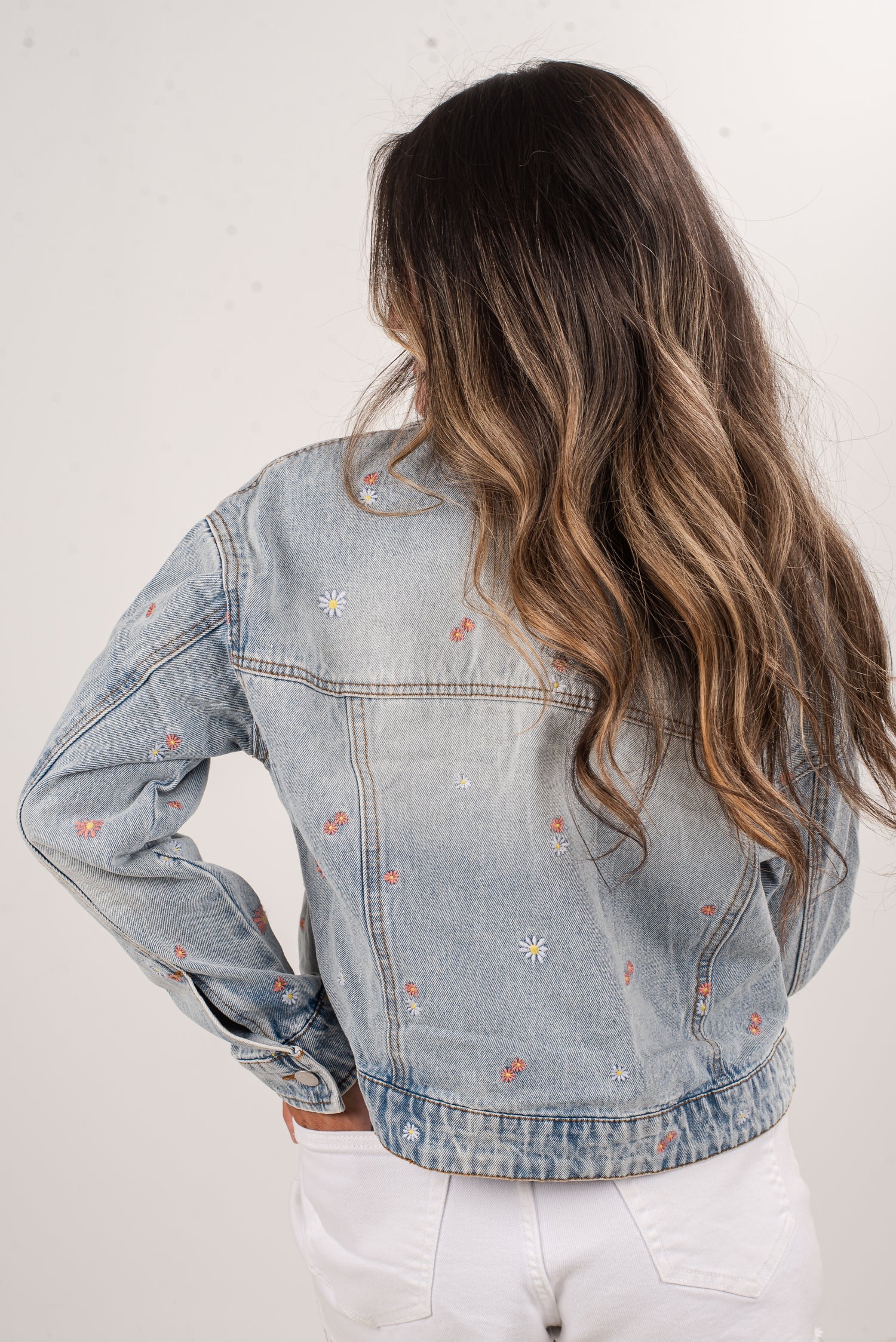 Person wearing a light blue denim jacket with floral embroidery on a white background