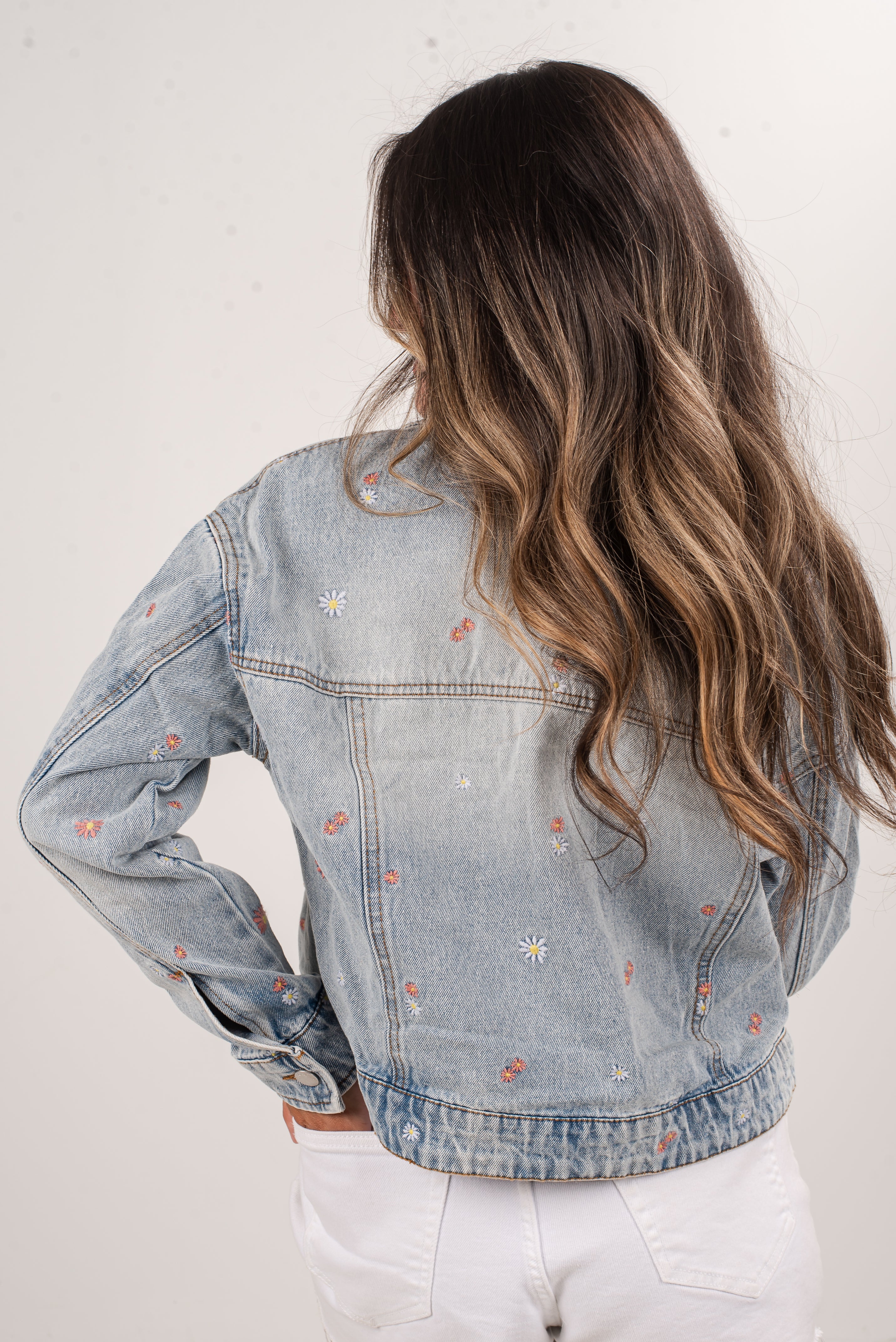 Person wearing a light blue denim jacket with floral embroidery on a white background