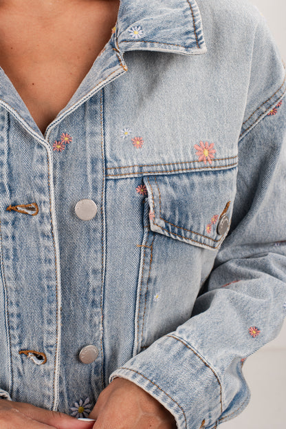 Light blue denim jacket with floral embroidery on a neutral background