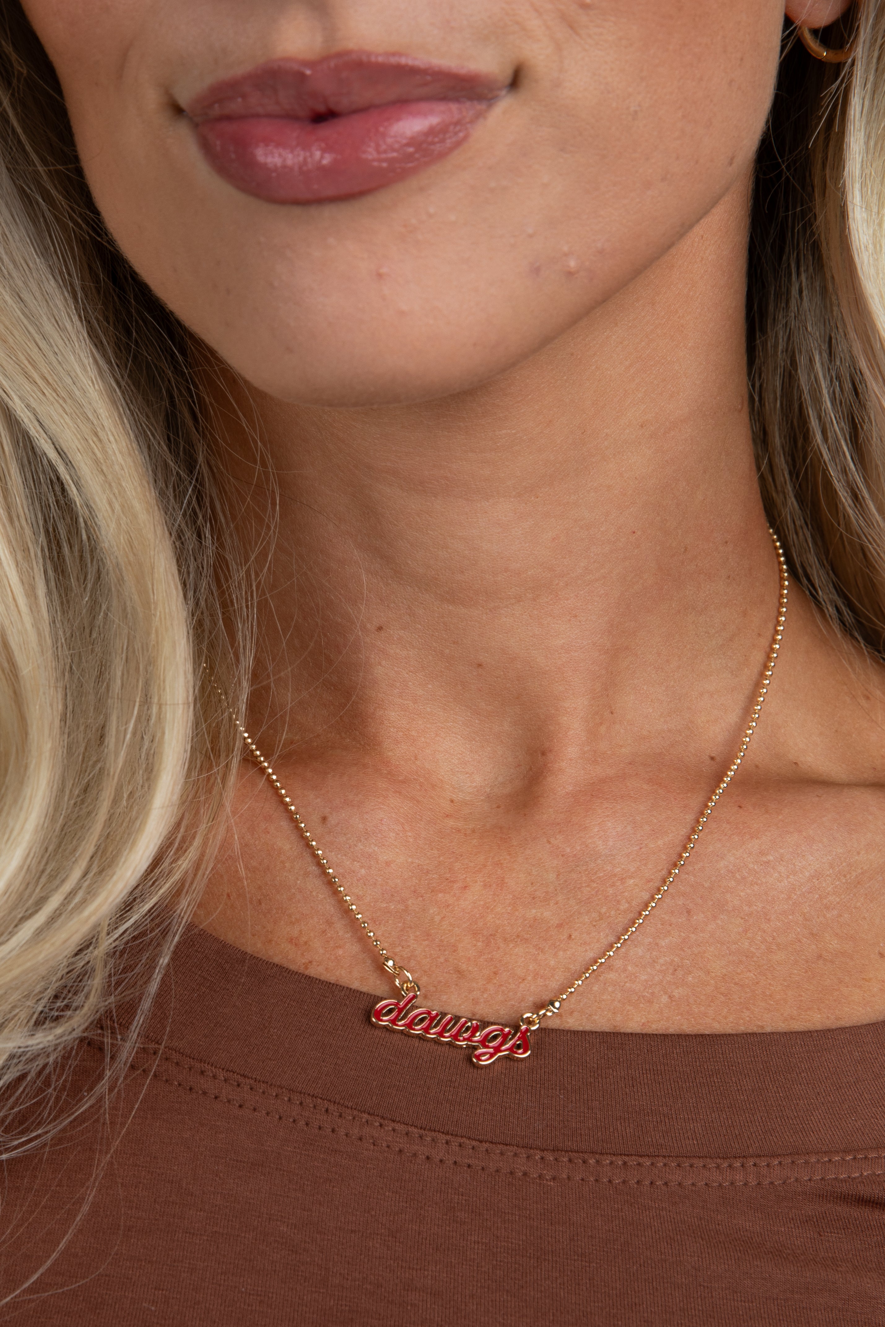Close-up of a person wearing a gold necklace with a red pendant.