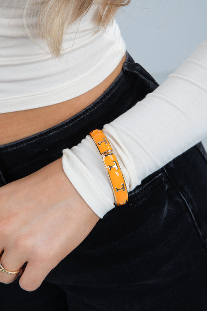 Person wearing a white long-sleeve top and black pants with an orange bracelet on a neutral background