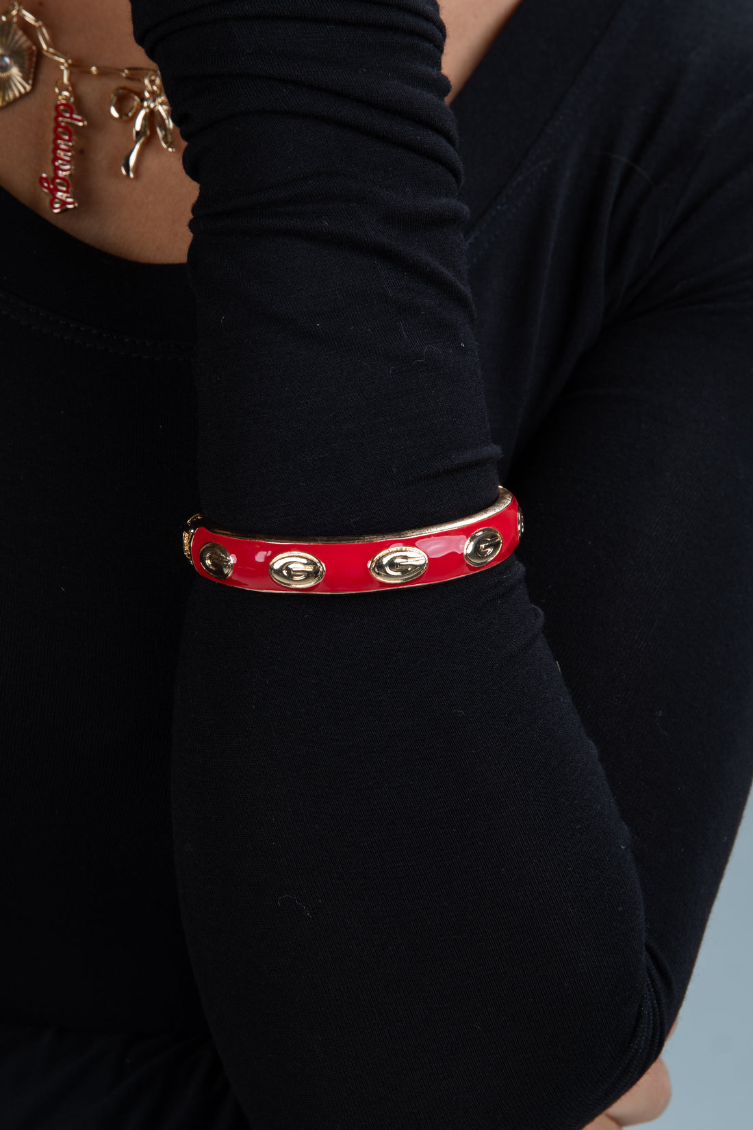 Red leather bracelet with gold accents on a person wearing a black long-sleeve shirt.