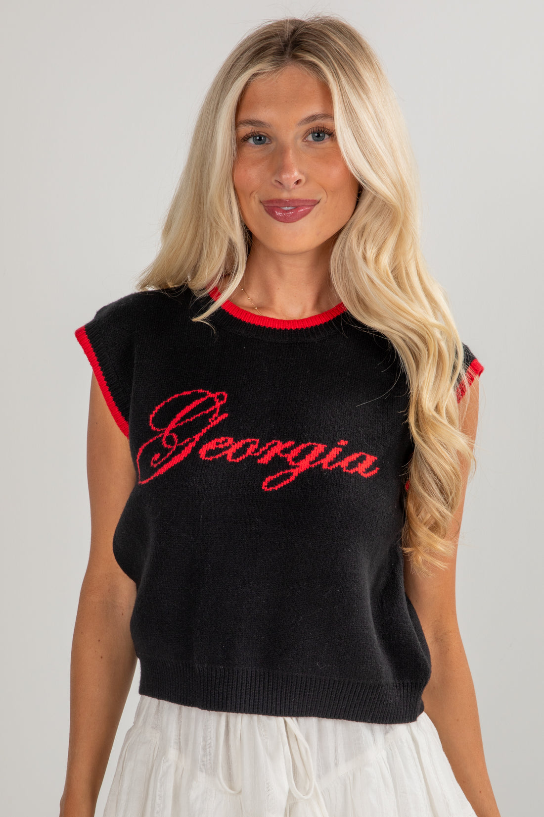 Woman wearing a black sleeveless top with red lettering on a plain background