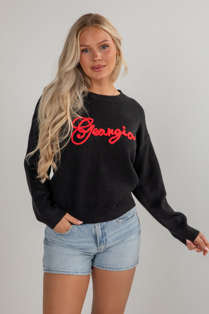 Woman wearing a black sweatshirt with red text and denim shorts on a plain background