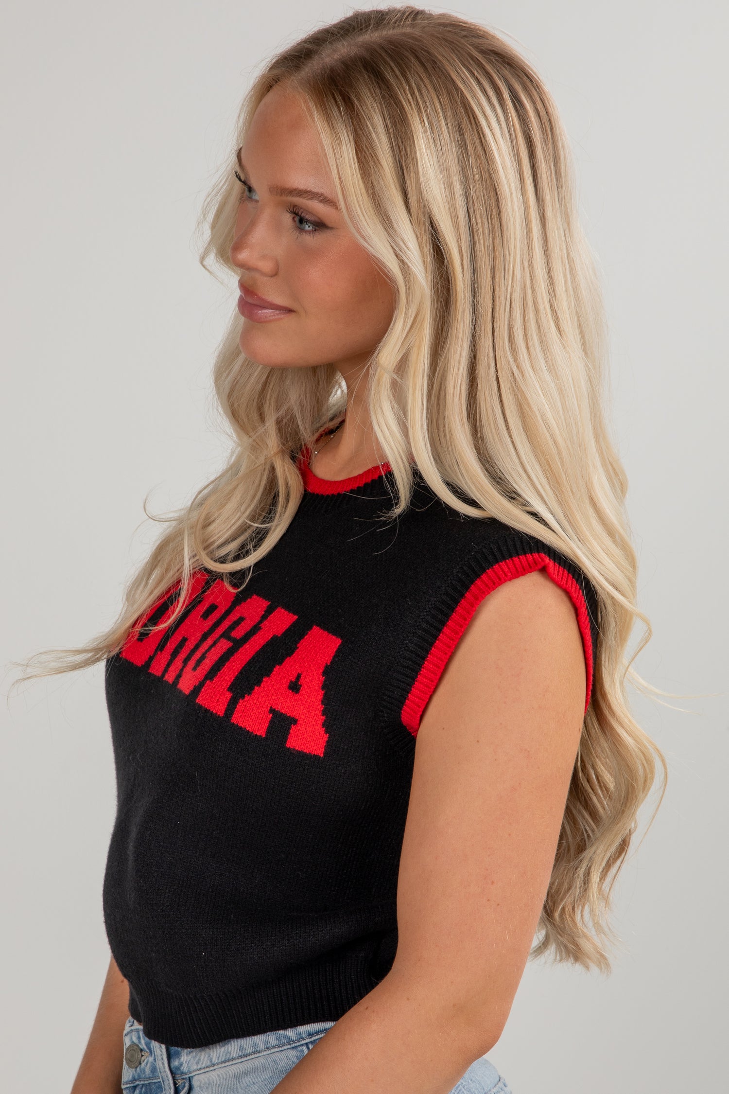 Woman wearing a black sleeveless top with red lettering against a plain background