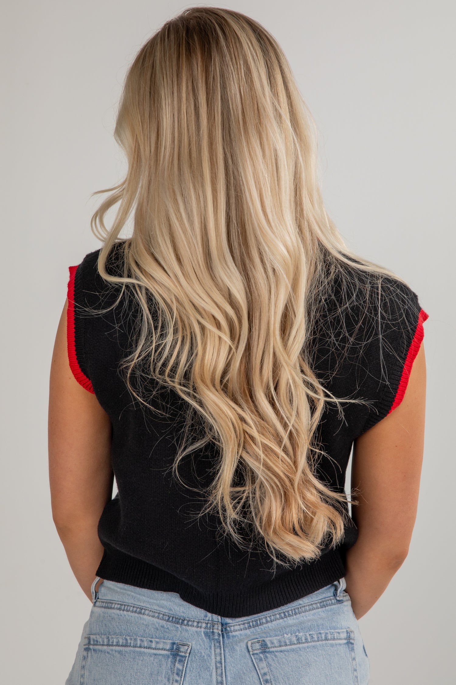 Person wearing a black sleeveless top with red trim and light blue jeans on a plain background