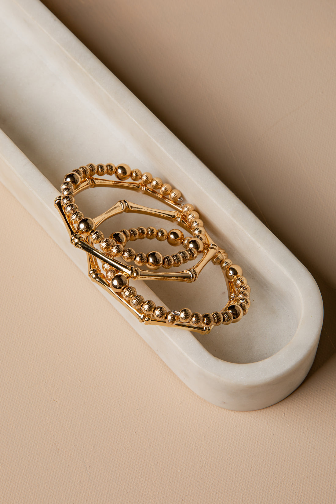 Three gold rings stacked on a white marble surface with a beige background