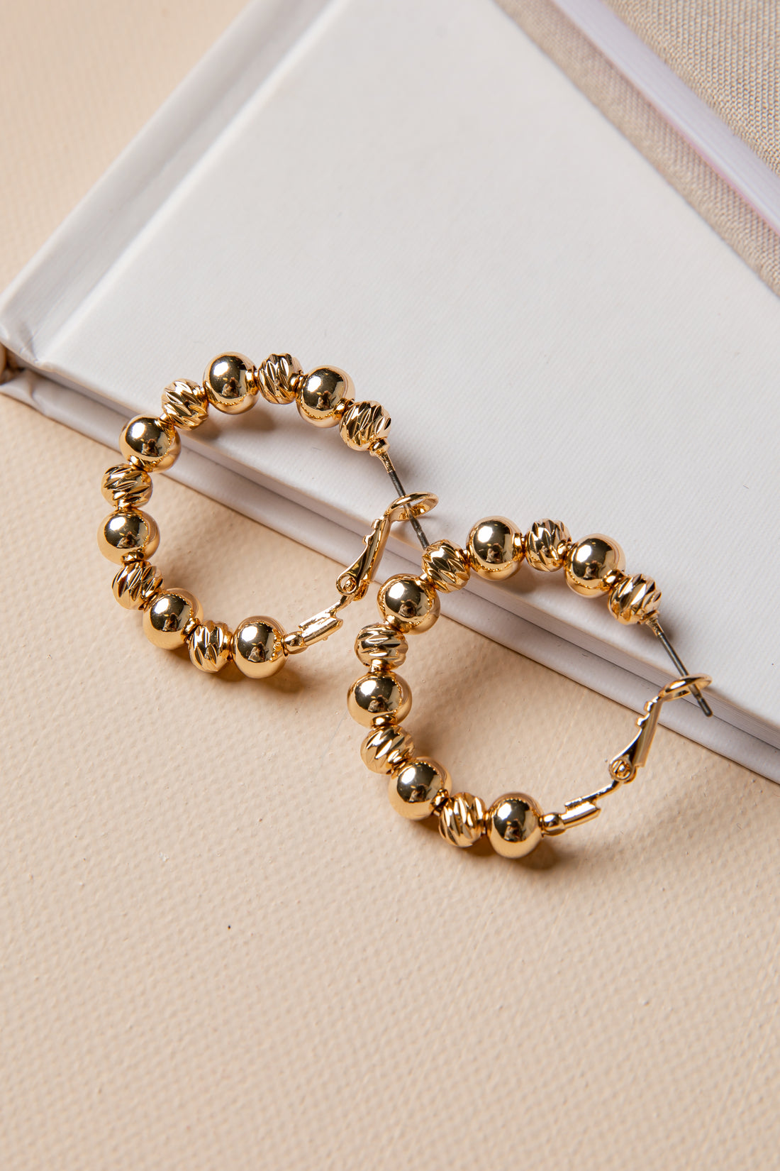 Gold hoop earrings with beaded design on a beige surface