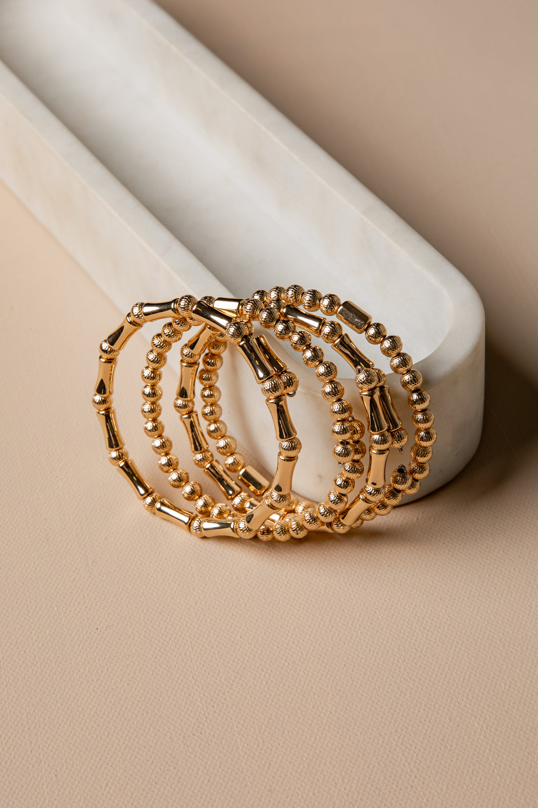 Gold hoop earrings on a marble stand with a beige background