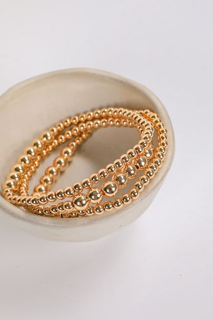 Three gold beaded bracelets on a white dish with a white background