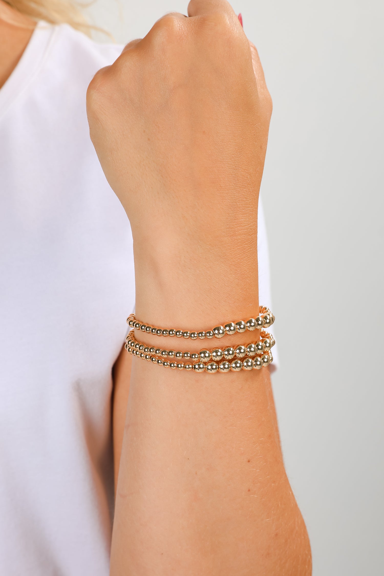 Close-up of a wrist wearing two gold bracelets on a plain background