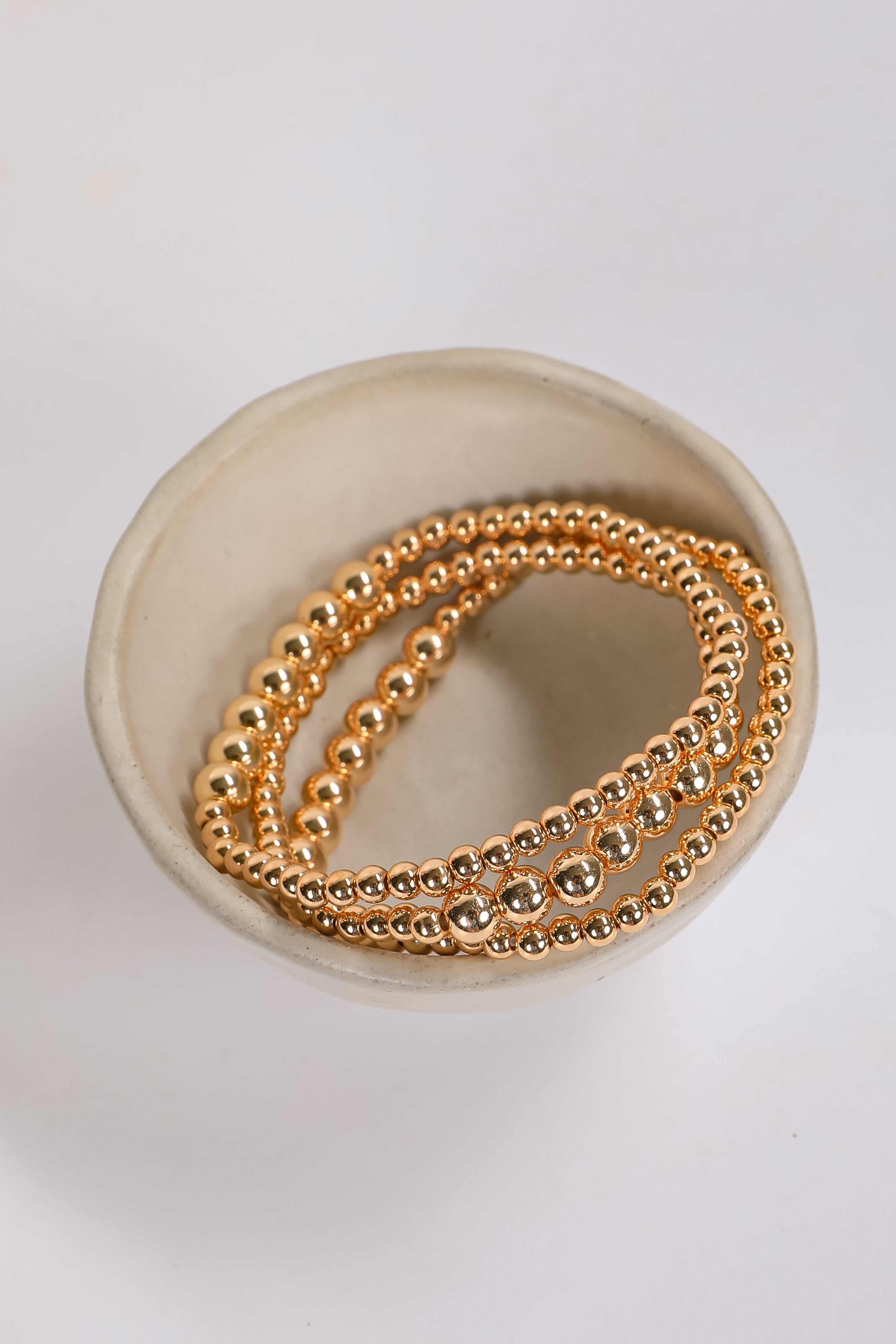 Gold beaded bracelets on a white dish with a white background