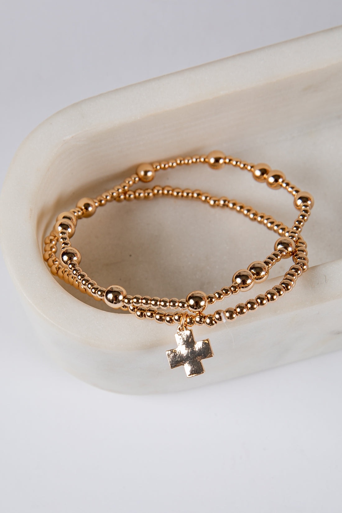 Gold beaded bracelet with a cross charm on a white surface
