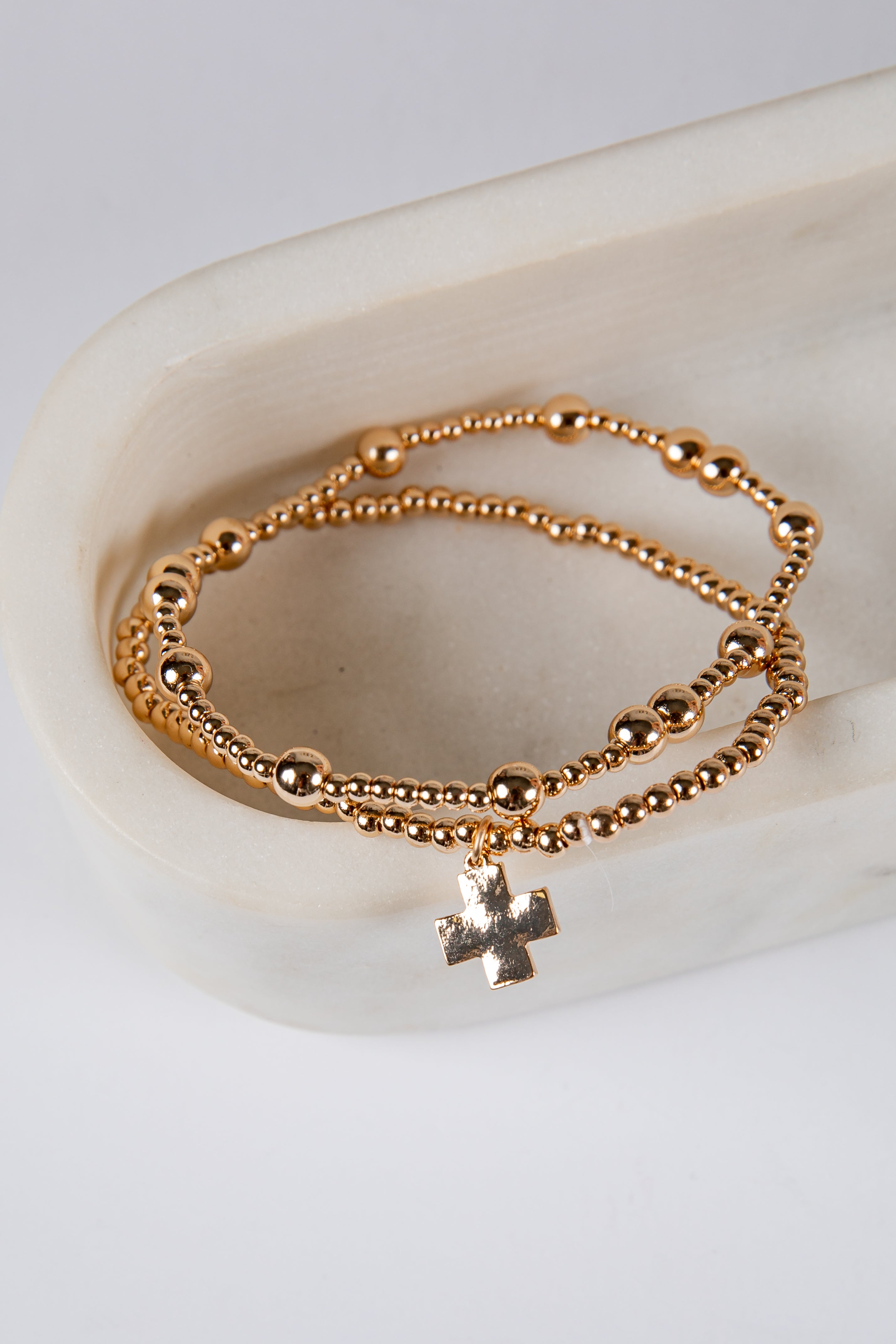 Gold beaded bracelet with a cross charm on a white surface