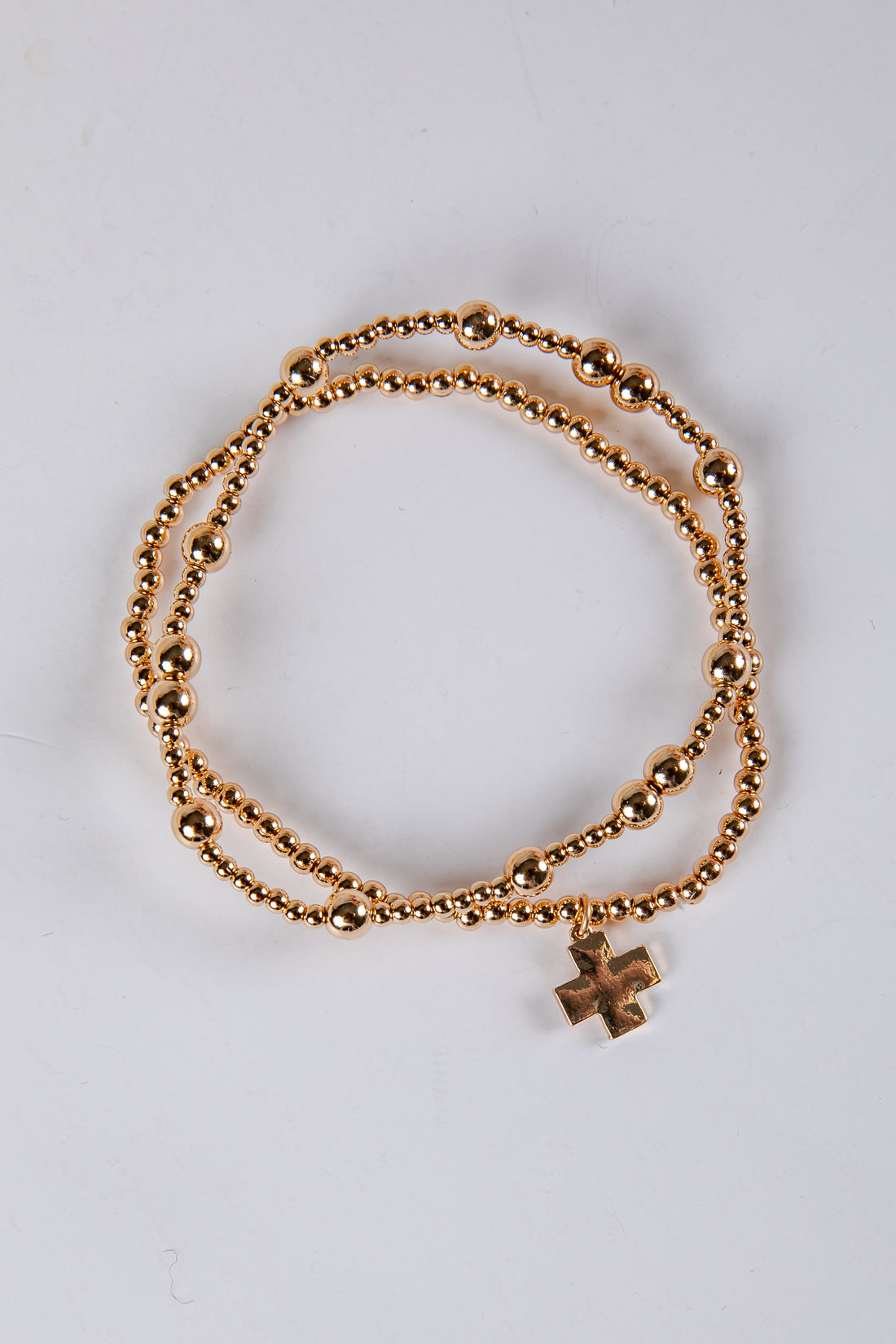 Gold bracelet with a cross charm on a light gray background