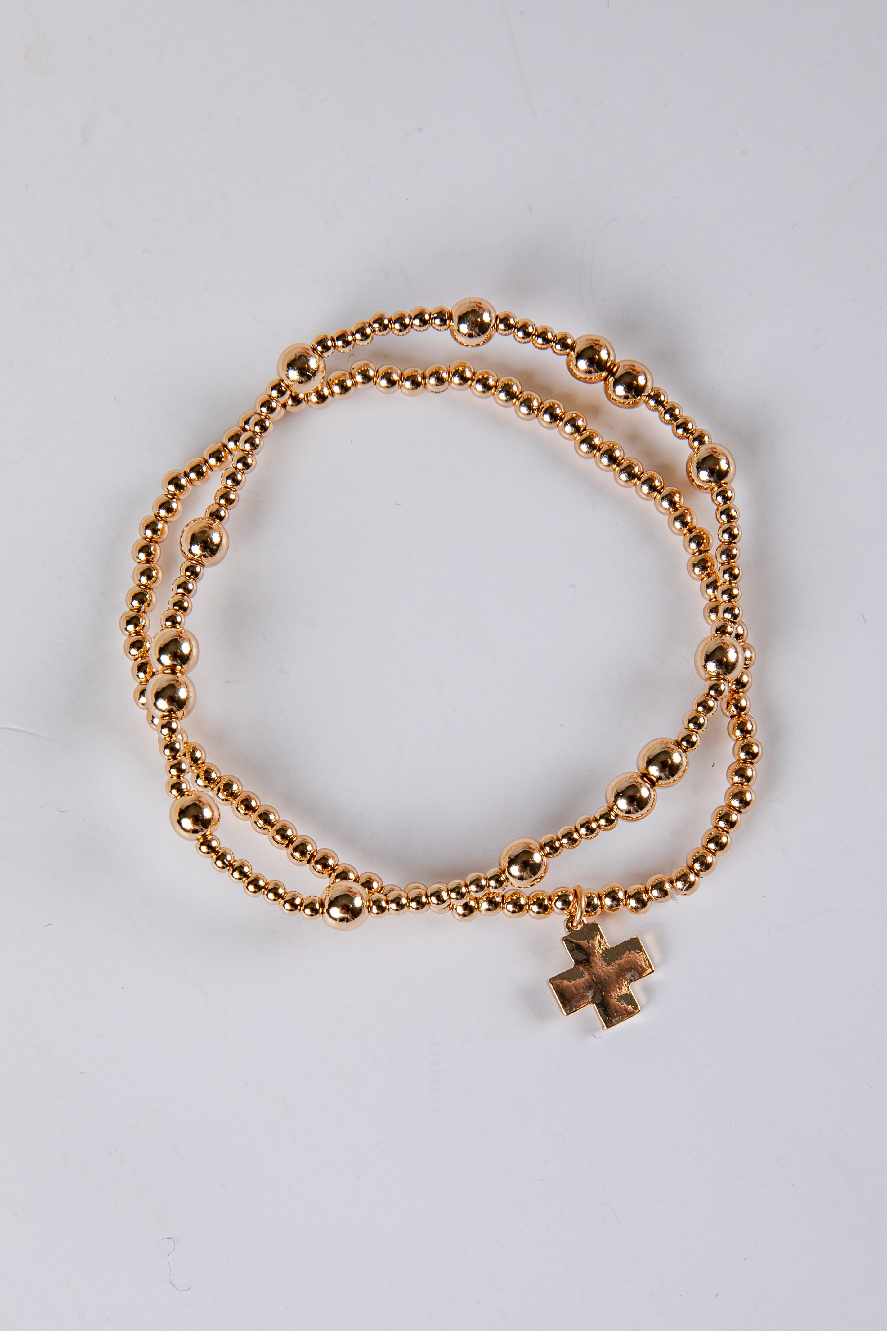 Gold bracelet with a cross charm on a light gray background
