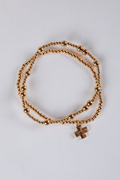 Gold bracelet with a cross charm on a light gray background