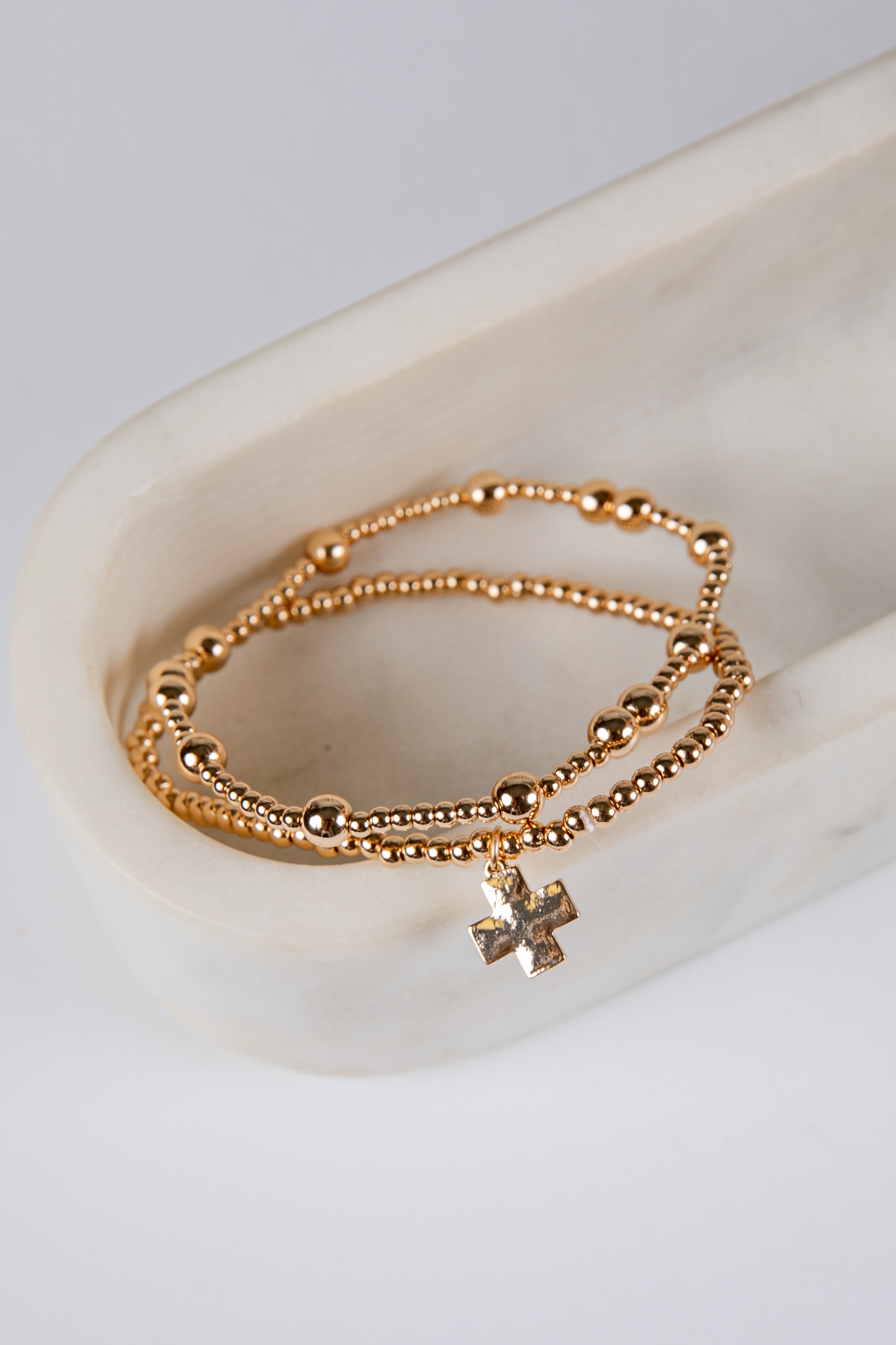 Gold bracelet with a cross charm on a white ceramic dish