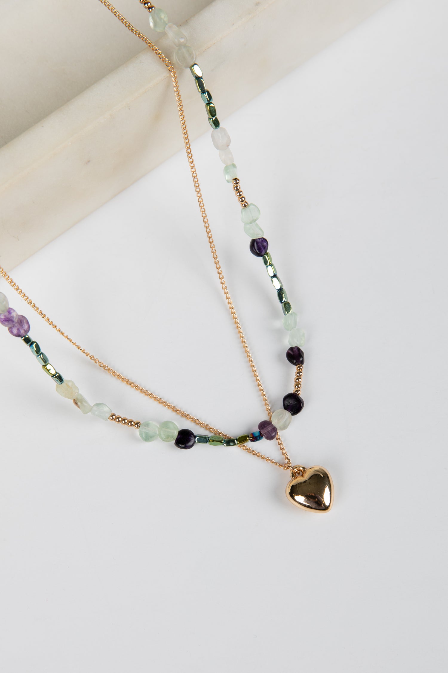 Layered beaded necklaces with a heart charm on a light background