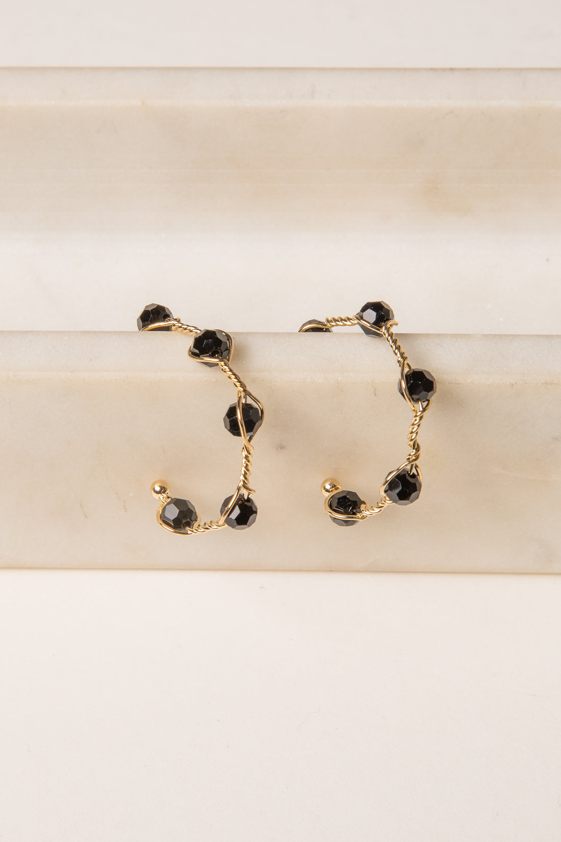 Gold hoop earrings with black gemstones on a beige surface