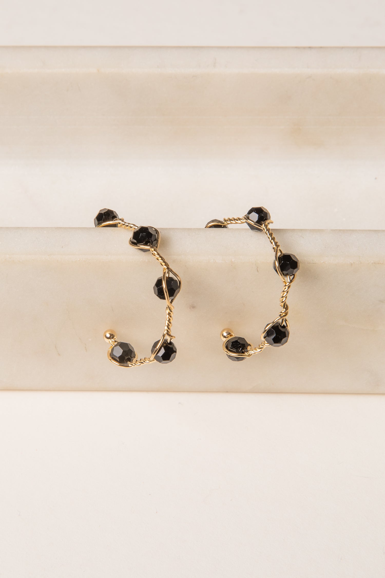 Gold hoop earrings with black gemstones on a beige surface