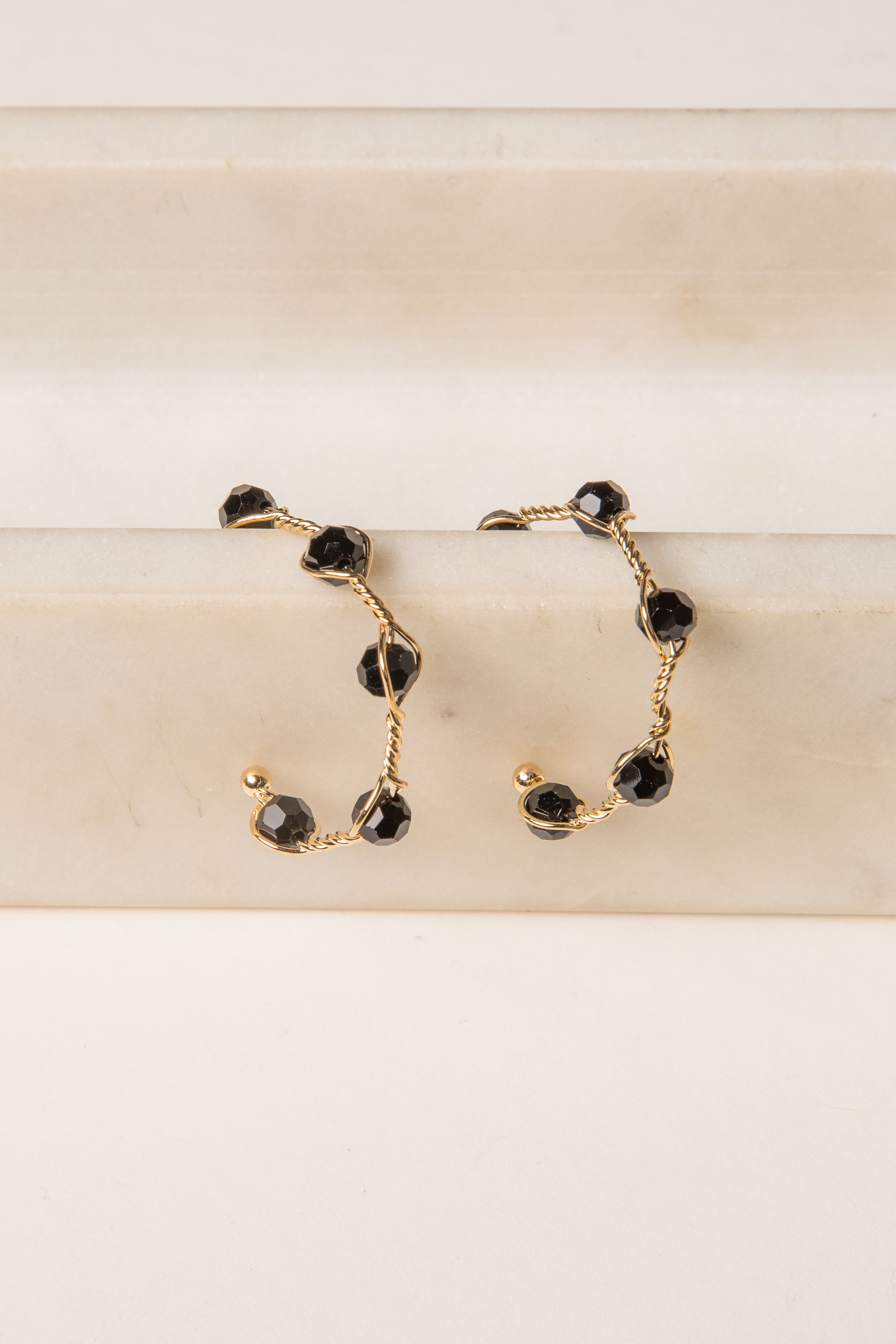 Gold hoop earrings with black gemstones on a beige surface