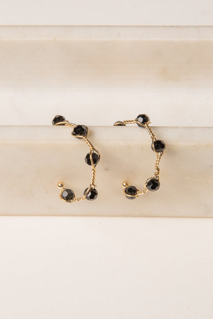 Gold hoop earrings with black gemstones on a beige surface