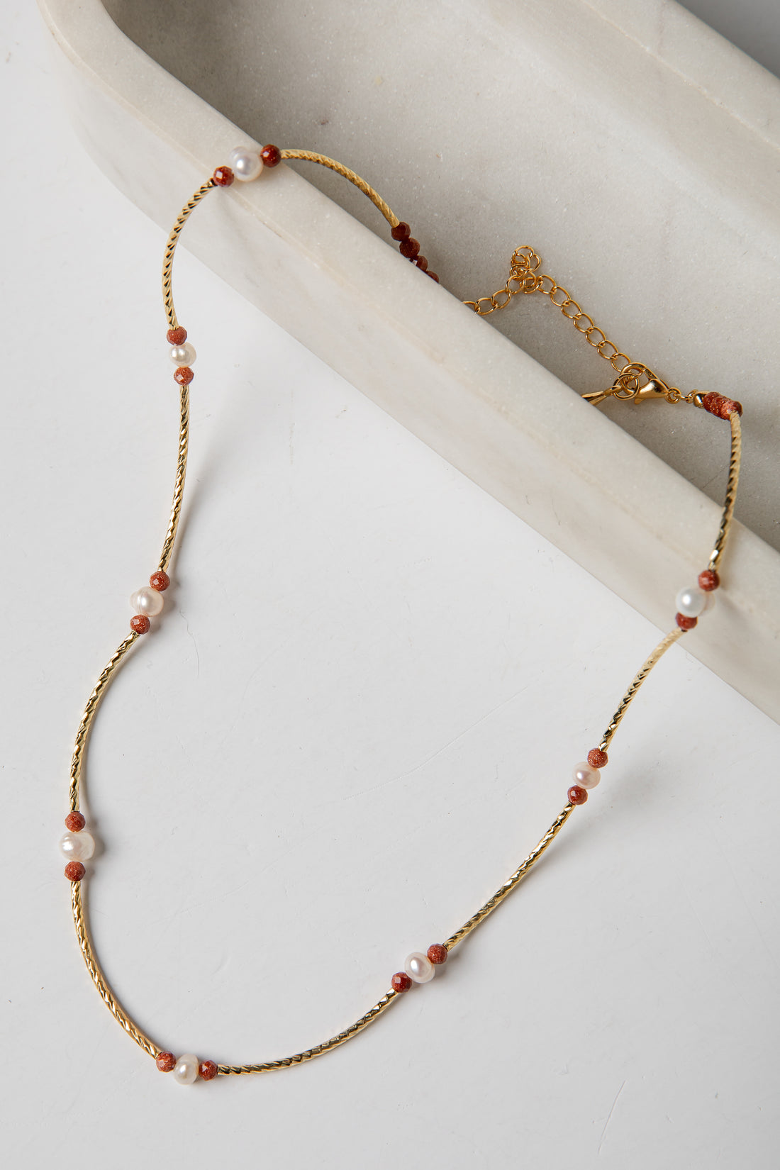 Necklace with gold chain and red and white beads on a light background