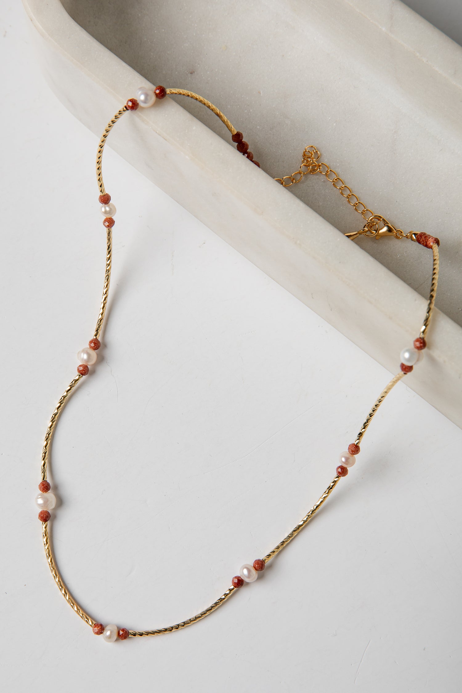 Necklace with gold chain and red and white beads on a light background